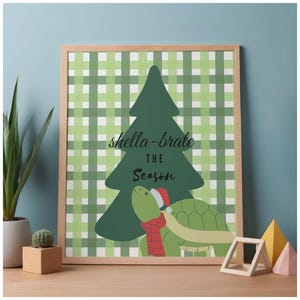 May include: A framed print with a green plaid background and a green Christmas tree silhouette. The print features a cartoon turtle wearing a Santa hat and scarf, with the text "shella-brate the season".