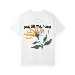 Peut inclure: T-shirt blanc avec un motif floral et du texte. Le motif présente une fleur jaune et orange avec des feuilles vertes, et les mots "PAS DE TAL POUR ST BARTH" en noir et bleu. Le texte "...ARE MADE OF FRANCE" est également inclus.