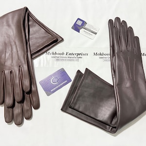 May include: A pair of dark brown leather gloves, laid out on a white surface. The gloves are long, with a smooth texture and visible stitching. Business cards with the text "Mehboob Enterprises Leather Gloves Manufacturer" are also present.