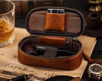 Puede incluir: Un estuche de cuero marrón con cremallera para pipas de tabaco y forro interior marrón oscuro. El estuche cuenta con un bolsillo para un encendedor de metal, una banda elástica para asegurar una pipa de madera oscura y un pequeño soporte.