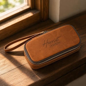 Puede incluir: Un estuche de cuero marr&oacute;n con cierre de cremallera y correa de mu&ntilde;eca. El nombre "Harriet Jackson" est&aacute; grabado en la parte delantera. El estuche rectangular parece ser de cuero de alta calidad.