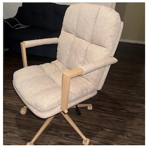 May include: Beige office chair with a padded seat and backrest. The chair has wooden armrests and a five-star base with wheels. The chair is designed for comfort and support, suitable for a home office or workspace.