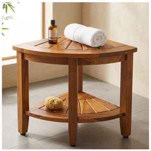 May include: A wooden corner shower bench with a natural finish. A rolled white towel and a brown bottle sit on the top shelf. A natural sponge rests on the lower shelf. The bench is designed for bathroom use.