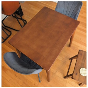 May include: A rectangular wooden dining table with a rich brown finish. The table has four tapered legs and a simple, elegant design. Two gray upholstered chairs and a small wooden stool are also visible.