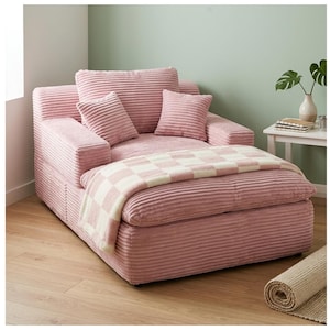 May include: A pink corduroy chaise lounge with matching pillows and a checkered blanket. The lounge has a wide seat and armrests. The room has a neutral color palette with a rolled rug on the floor.