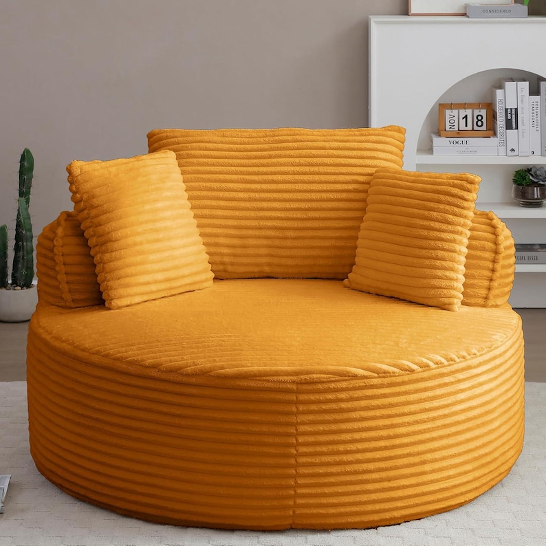 Puede incluir: Un sof&aacute; redondo de pana amarillo mostaza con cojines a juego. El sof&aacute; tiene un perfil bajo y un asiento ancho y circular. El respaldo es un coj&iacute;n grande y rectangular, y hay cuatro cojines cuadrados m&aacute;s peque&ntilde;os. El sof&aacute; est&aacute; dise&ntilde;ado para la comodidad.