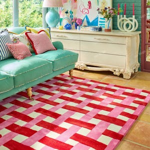 Può includere: Un vivace tappeto rettangolare con un motivo intrecciato a strisce rosse, rosa e bianco sporco. Il tappeto è posato su un pavimento piastrellato e si trova in una stanza con un divano turchese e una cassettiera bianca. Il tappeto è etichettato "Jav Rugs".