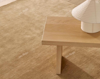 Puede incluir: Una alfombra marrón claro con una mesa de madera a juego y una lámpara de papel blanca. La alfombra tiene un aspecto texturizado. La mesa tiene un diseño sencillo con una sola pata. La lámpara tiene forma cónica.