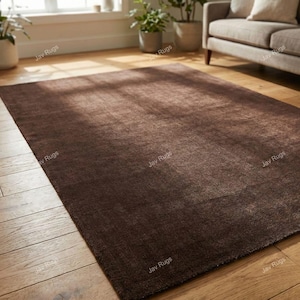 May include: A rectangular, dark brown rug with a textured surface. The rug is placed on a hardwood floor, and the overall aesthetic is warm and inviting. The rug is a solid color and appears to be made of a soft material.