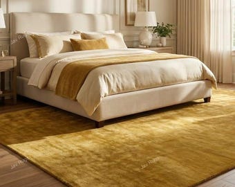 Puede incluir: Una habitación con una cama con ropa de cama color crema y una colcha color mostaza. Una gran alfombra color mostaza cubre el suelo. La habitación está bien iluminada y una lámpara está sobre una mesita de noche.