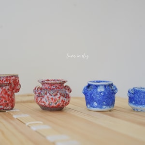 May include: A set of three ceramic mugs with a speckled, matte finish. Each mug features a different color: light blue, cream, and gray. The mugs have a simple, modern design and a comfortable handle.