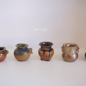 May include: A white ceramic mug with a black handle and the text "But First, Coffee" in a bold, black font. The mug is set against a blurred background, suggesting a cozy setting.