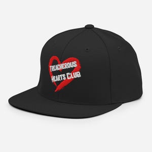 Può includere: Cappellino da baseball nero con visiera piatta. Il cappellino presenta la scritta "TREACHEROUS HEARTS CLUB" ricamata in bianco su un cuore rosso.