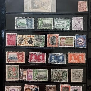 May include: A collection of vintage postage stamps from various countries arranged in a black display album. The stamps feature diverse portraits, landscapes, and historical imagery with various denominations and text in multiple languages.