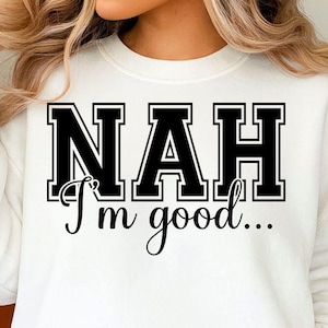 Peut inclure: Sweat-shirt blanc avec l'inscription "NAH I'm good..." en noir. Le texte est en lettres majuscules grasses et en cursive. Le sweat-shirt est de style col rond et est porté avec un jean bleu, pour un look décontracté.