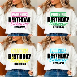 May include: A white long-sleeve sweatshirt featuring the text WARNING BIRTHDAY BEHAVIOR IN PROGRESS in four color variations: pink, green, yellow, and blue. The word WARNING is in a colored box, BIRTHDAY is in bold black, and BEHAVIOR is in script.