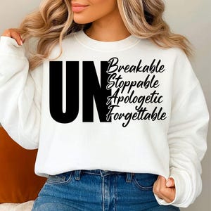 May include: White sweatshirt with the word "UN" in large black letters, followed by the words "Breakable, Stoppable, Apologetic, Forgettable" in a script font. The sweatshirt is paired with blue jeans.