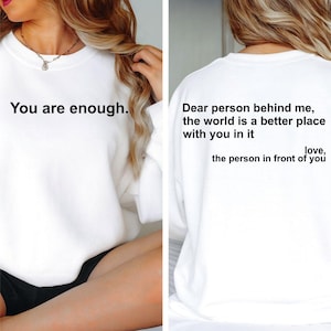 May include: White sweatshirt with the text "You are enough" on the front. The back of the sweatshirt has the text "Dear person behind me, the world is a better place with you in it love, the person in front of you."