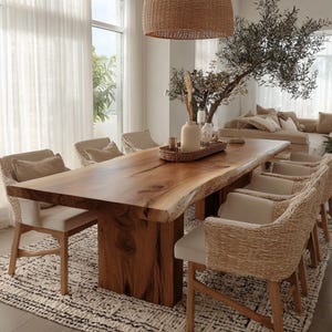 Pode incluir: Uma grande mesa de jantar de madeira natural com borda viva, sustentada por uma base de madeira maci&ccedil;a. Oito cadeiras tecidas com almofadas creme circundam a mesa. O ambiente apresenta uma paleta de cores neutras, uma lumin&aacute;ria tecida e um tapete estampado.