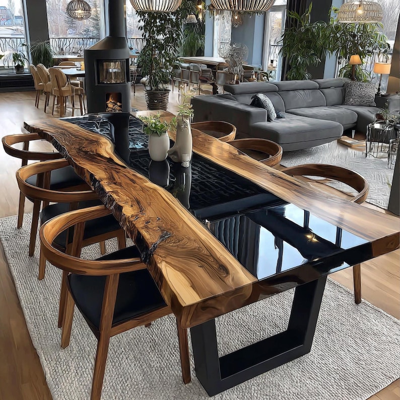 Op de afbeelding: Een grote, moderne eettafel met een houten blad met een levende rand en een zwart epoxyhars midden. De tafel wordt ondersteund door een zwart metalen onderstel en is omringd door houten stoelen met zwarte leren zittingen. De tafel is ongeveer 305 cm lang.