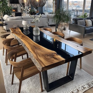 Op de afbeelding: Een moderne eettafel met een houten blad met levende rand en een zwart epoxyhars middenstuk. De tafel wordt ondersteund door zwarte metalen poten. Houten stoelen omringen de tafel. De kamer heeft een neutraal kleurenpalet.