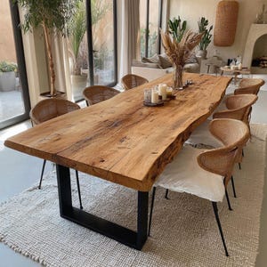 Puede incluir: Una gran mesa de comedor de madera natural con borde vivo, sostenida por una base de metal negro. Alrededor de la mesa hay sillas de mimbre tejido con patas de metal negro. La mesa está decorada con velas y un jarrón con flores secas.