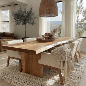 Pode incluir: Uma mesa de jantar de madeira clara com borda natural, rodeada por cadeiras estofadas creme. Um tapete tecido e uma lumin&aacute;ria pendente tecida contribuem para a est&eacute;tica natural da sala. Objetos decorativos est&atilde;o sobre a mesa.