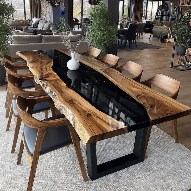 Op de afbeelding: Een grote, rechthoekige eettafel met een houten blad met levende rand en een zwart epoxyhars midden. De tafel wordt ondersteund door een zwarte metalen basis en is omgeven door houten stoelen met zwarte zittingen. De tafel is ongeveer 254 cm lang.