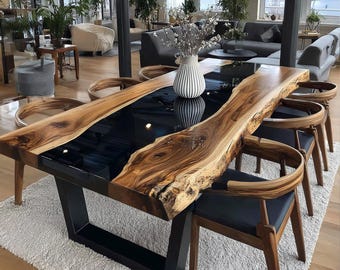May include: A large, live edge wooden dining table with a black epoxy resin center. The table is supported by a black metal base and surrounded by wooden chairs with black leather seats. A white vase with flowers sits on the table.