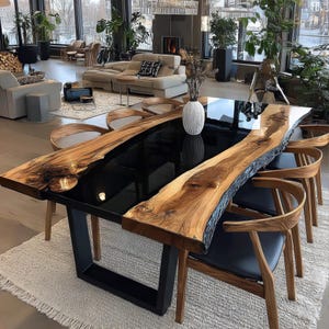 Op de afbeelding: Een grote, moderne eettafel met een zwart epoxy middenstuk en zijkanten van levend hout. De tafel wordt ondersteund door een zwarte metalen basis en is omringd door houten stoelen met zwarte zittingen. De tafel is ongeveer 254 cm lang.