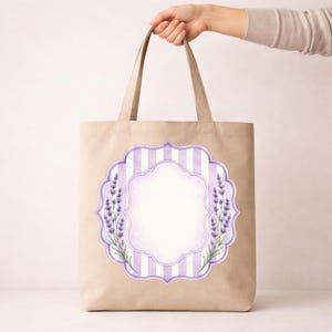 May include: A beige tote bag featuring a central decorative label design. The graphic includes vertical light purple and white stripes, a scalloped frame, and watercolour-style lavender sprigs on the left and right sides of the blank centre.