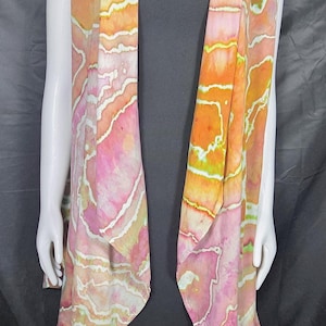 May include: A sleeveless waistcoat featuring a tie-dye pattern in shades of orange, pink, and yellow with white wavy lines throughout. The garment has an open front design with a draped collar and falls to a mid-thigh length over a black base layer.
