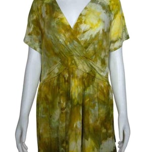 May include: A short-sleeved top featuring a v-neckline and a wrap-style front with a gathered waist. The garment displays a tie-dye pattern in shades of olive green, mustard yellow, and white, creating a mottled, blended appearance across the fabric.
