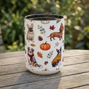 May include: A white ceramic mug featuring a repeating pattern of dogs in sweaters, including a French Bulldog, a Dachshund, an Australian Shepherd, and a Boston Terrier, interspersed with autumn elements like pumpkins, acorns, and fall leaves.