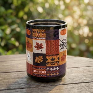 May include: A black ceramic mug featuring a patchwork design of autumn and Halloween motifs. The pattern includes orange pumpkins, brown maple leaves, a white ghost, a black spider web, and various knit-style textures in shades of orange and purple.