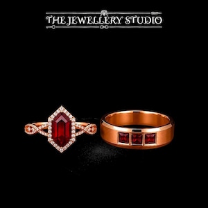 Peut inclure: Un ensemble de bagues en or rose comprenant une pierre rouge hexagonale entourée de petites pierres blanches sur un anneau torsadé, et une alliance en or rose avec trois pierres rouges carrées. Le texte THE JEWELLERY STUDIO est visible.