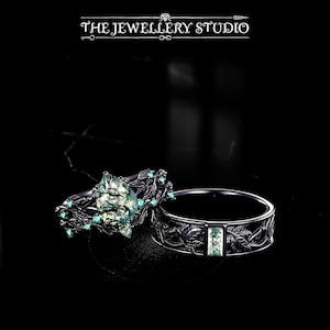 May include: Two rings with a dark metal finish. One ring features a large, textured, light green stone with smaller green stones. The other ring has a band with a leaf design and a rectangular green stone. The Jewellery Studio logo is at the top.