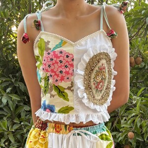 May include: A patchwork dress with a floral print bodice and a white lace skirt. The bodice features a mix of floral patterns and a decorative oval patch. The skirt has a white lace overlay with a ruffled hem.