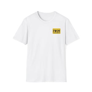 May include: A white short-sleeve t-shirt featuring a small rectangular yellow graphic on the left chest. The graphic has a black border and contains the text I'M 21! in bold black letters, with the words PROFESSIONAL DRINKING PLAYER below it.