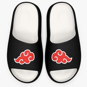 May include: A pair of black slide sandals featuring a white interior lining and a prominent red cloud graphic with a white outline on the top of each strap. The footwear has a rounded toe design and a smooth, solid black exterior finish.