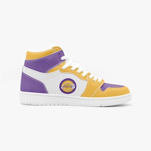 May include: High-top sneaker in Los Angeles Lakers team colors. The shoe features a white base with purple and gold accents, a Lakers logo, and white laces. The sole is white.