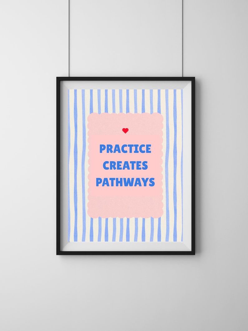 May include: A framed art print with a black frame. The artwork features a light blue and white striped background. A pink, scalloped-edge shape in the center contains the words "PRACTICE CREATES PATHWAYS" in blue, with a red heart above.