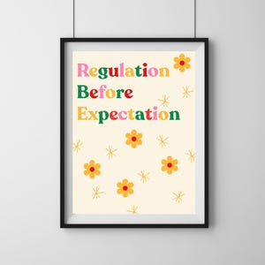 Op de afbeelding: Ingelijste kunstdruk met de woorden "Regulation Before Expectation" in kleurrijke tekst. De print heeft een crèmekleurige achtergrond met oranje bloemen en gouden sterren. De lijst is zwart.