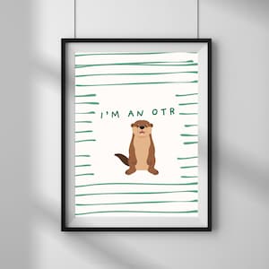 May include: Framed art print featuring a cartoon otter with the text "I'M AN OTR" in green. The otter is brown and tan, standing upright on a white background with green horizontal lines. The frame is black.