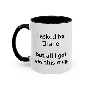 May include: White ceramic mug with a black handle and interior. The mug features the text "I asked for Chanel but all I got was this mug" in black lettering. A humorous gift idea.