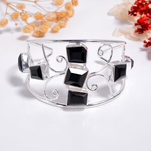 May include: A silver cuff bracelet featuring a series of faceted black square stones set within a delicate openwork frame of swirling metal wire. The design includes multiple black stones arranged along the front and sides of the polished silver band.