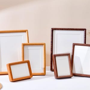Può includere: Una collezione di sei cornici rettangolari in legno di varie dimensioni e due diverse tonalità di legno. Tre cornici presentano una finitura in legno naturale chiaro, mentre le altre tre sono realizzate in legno marrone scuro, tutte con passe-partout bianco.