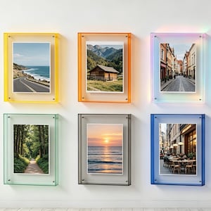 May include: Six rectangular wall-mounted picture frames with translucent acrylic borders in yellow, orange, iridescent, green, grey, and blue. Each frame displays a different landscape or urban photograph, including coastal roads, mountains, and city streets.