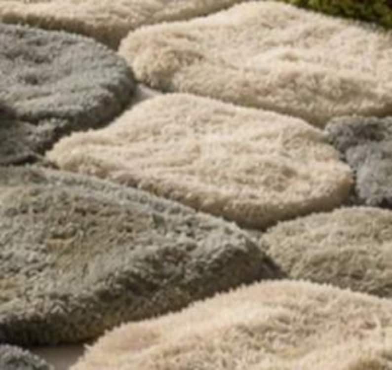 May include: Close-up of a textured rug with a stone-like pattern. The rug features various shades of gray and beige, creating a natural, organic look. The design resembles stepping stones or cobblestones, adding a touch of rustic charm to any space.