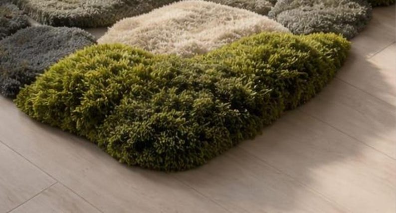 May include: A multi-colored rug with a shaggy texture. The rug features a combination of green, beige, and gray sections, creating a textured, organic appearance. The rug is placed on a light-colored wooden floor.